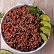 A white bowl with black beans risotto with red peppers and lime wedges.