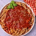 A white bowl with pasta and tomato sauce.