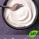 A bowl filled with vegan sour cream with a spoon with a text overlay of recipe title.