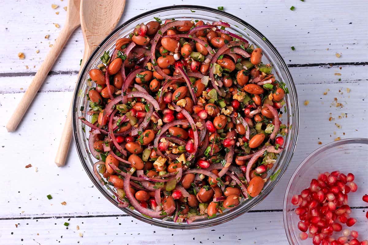 Borlotti bean salad with pomegranate arils in a bowl and wooden spoons.