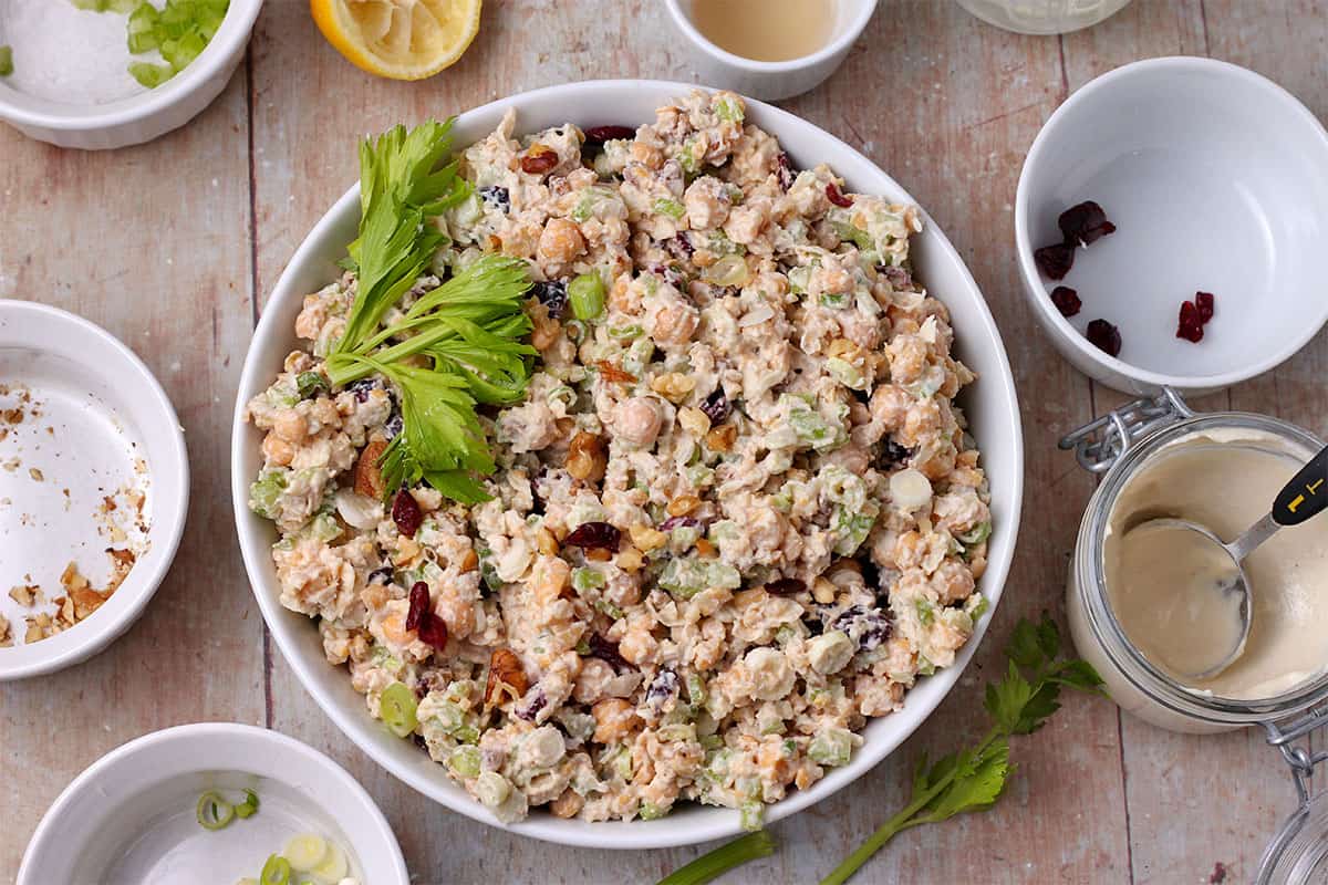 A white bowl filled with chickpea salad with scallions, walnuts, dried cranberries, and celery.