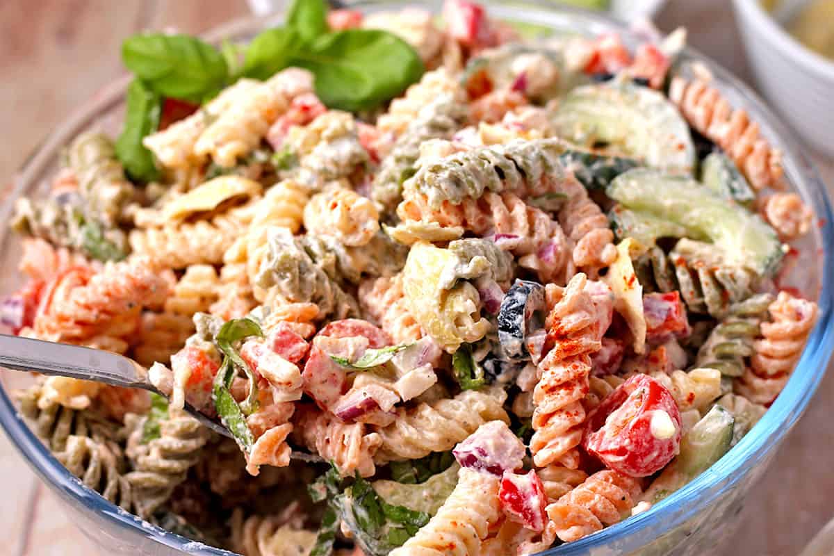 Creamy pasta salad with black olives is mixed with a spoon.