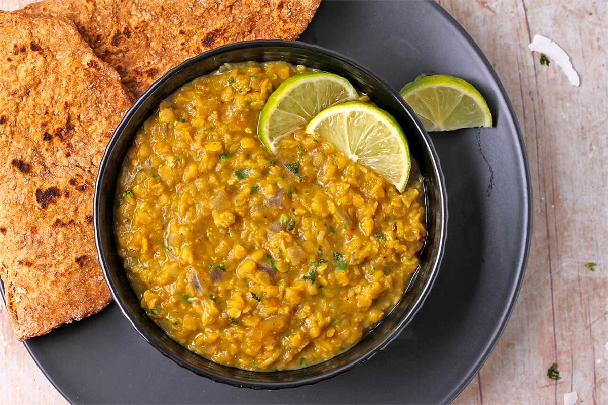 Mango dahl in a black bowl with lime wedges.