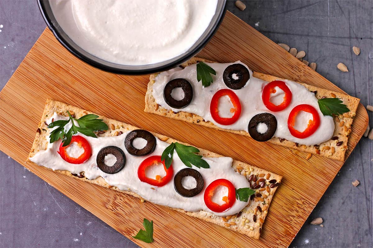 Crackers with sour cream, olive slices, and chili slices on them.