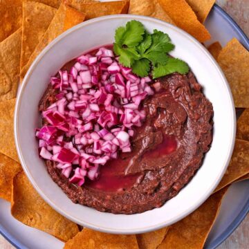A bowl of black bean dip with red onions and tortilla chips.