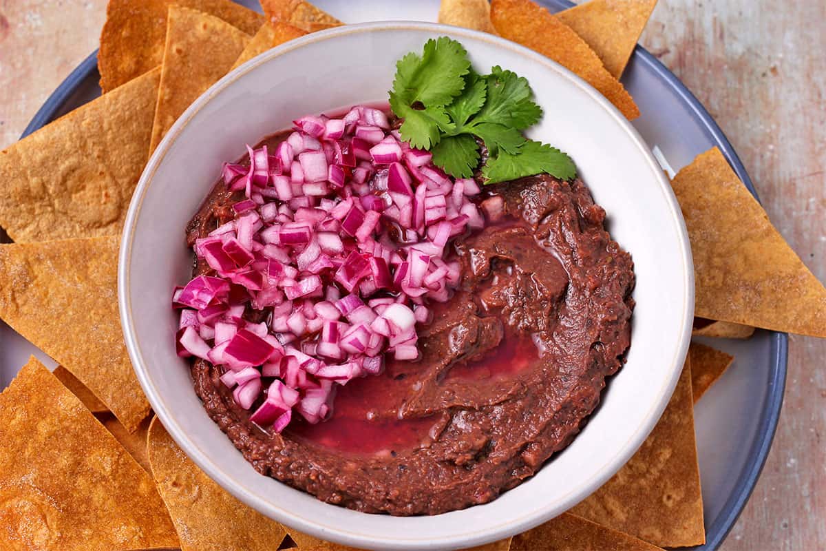 Black bean dip with red onions and cilantro on a plate with tortilla chips.