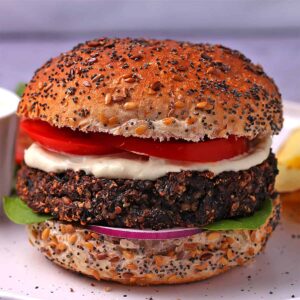 A mushroom burger in a bun with mayo, lettuce, tomato slices, and red onion.