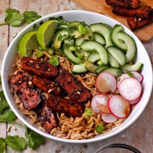 A bowl with noodles, baked tofu, radishes, cucumber, scallions, cilantro, and limes.