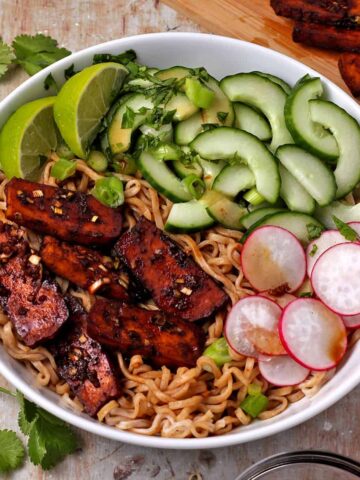 A bowl with noodles, baked tofu, radishes, cucumber, scallions, cilantro, and limes.