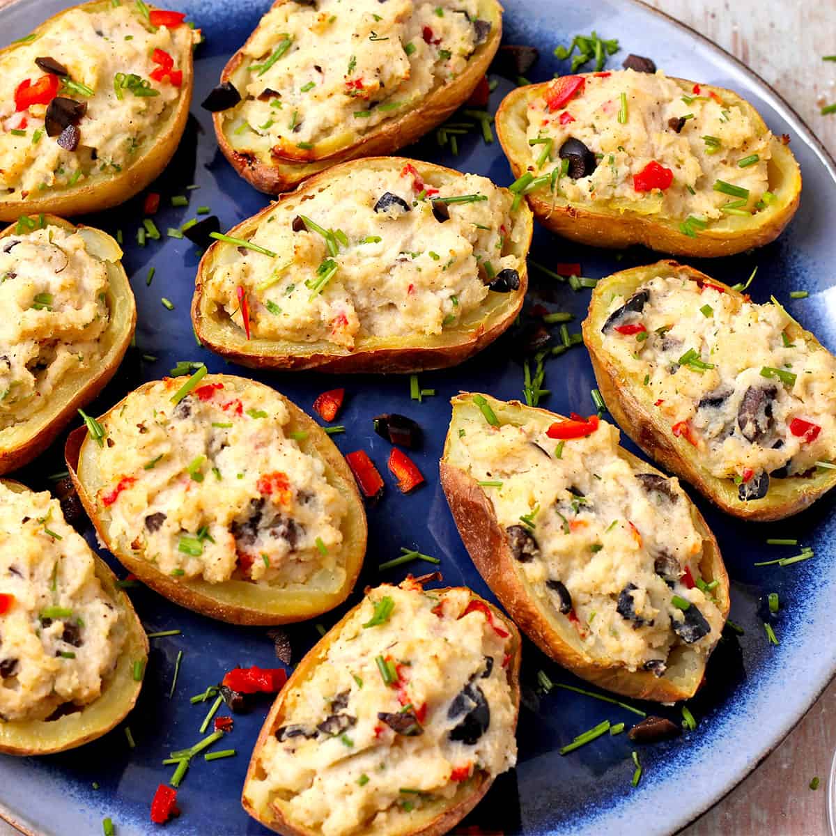 Twice-baked potatoes halves with black olives, chives, and red chili on a blue plate.