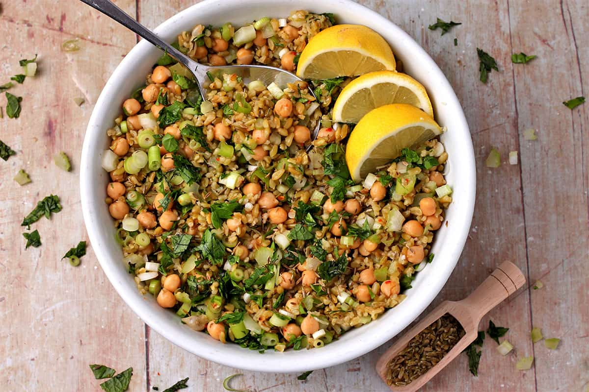 freekeh salad with chickpeas, fresh herbs, celery, scallions, and lemons in a bowl.