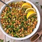 A white bowl filled with lemon freekeh salad with herbs, chickpeas, celery, scallions, and cumin seeds.