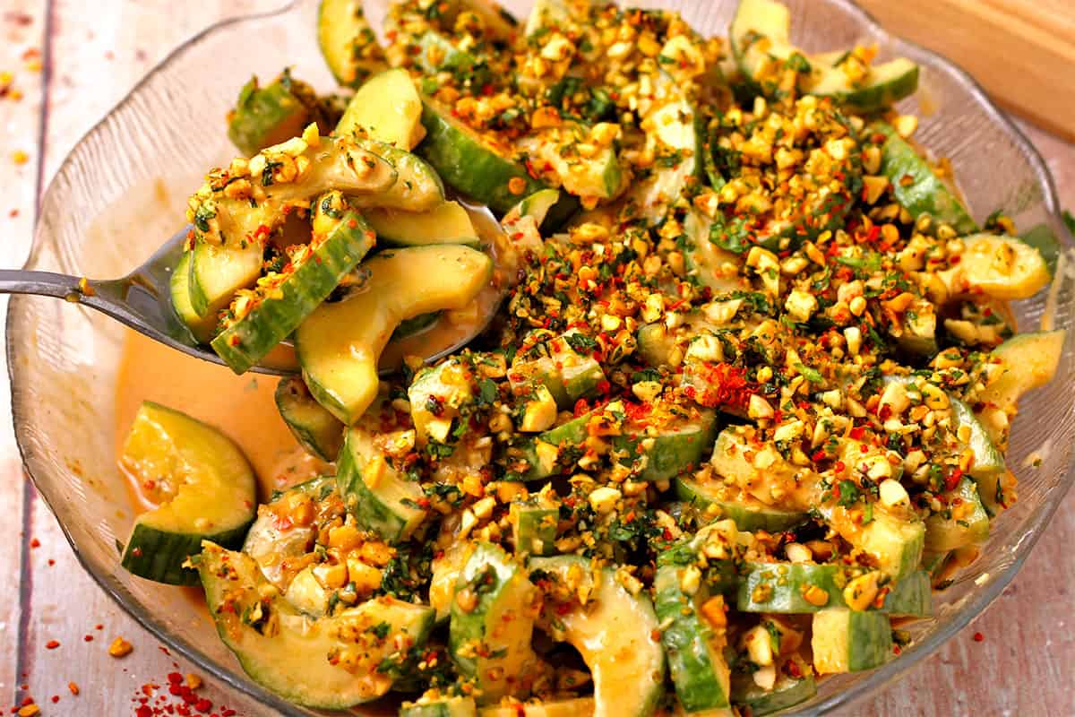 A spoonful of cucumber salad with peanut dressing, red chili flakes, peanuts, and chopped cilantro.