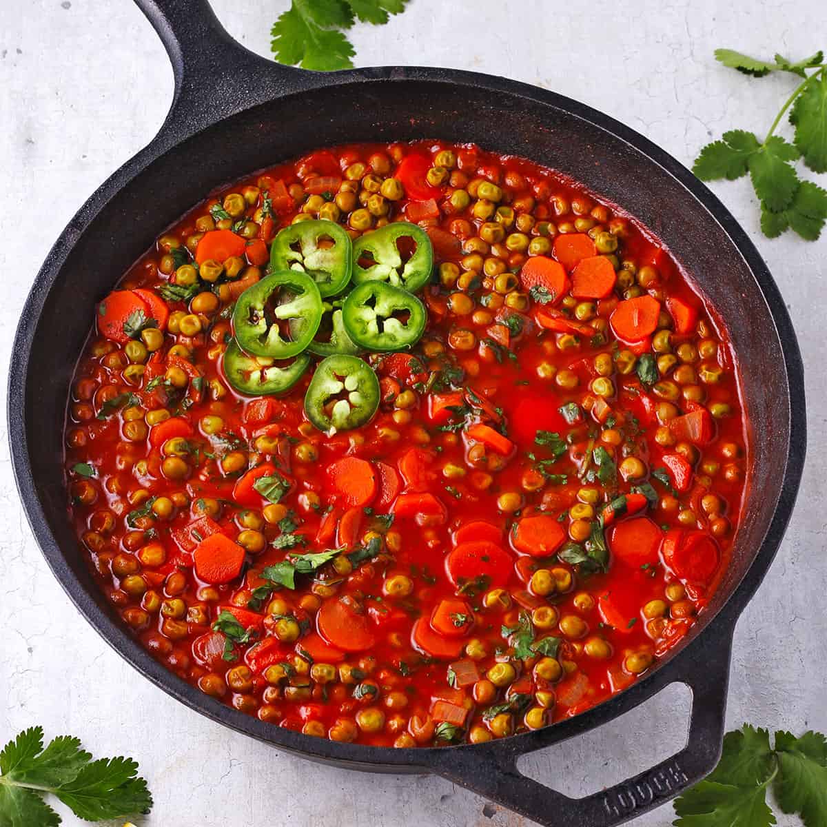 Pea stew with carrots in tomato sauce in a black pan.