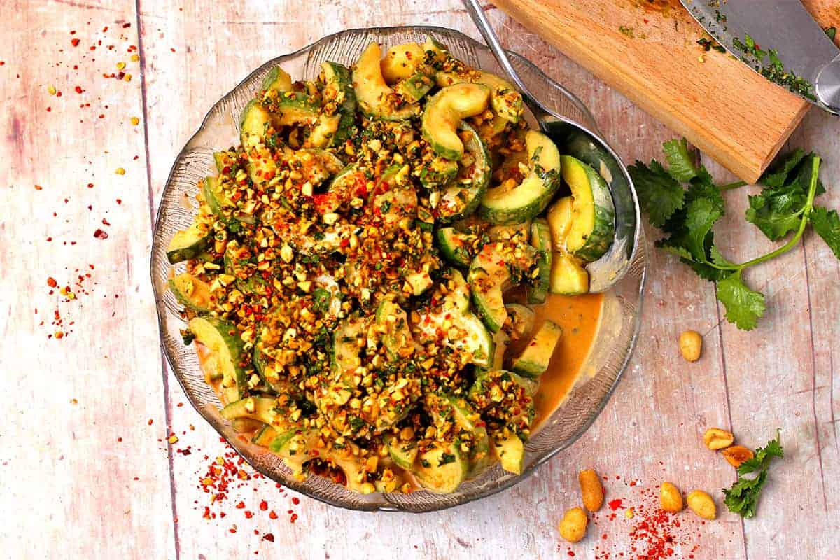 A glass dish with sliced cucumbers, peanut dressing, and spice mix.