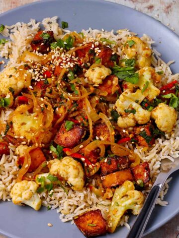 A plate with stir-fried cauliflower and tofu over rice.