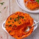 A bowl of creamy sweet potato dip topped with chopped parsley.