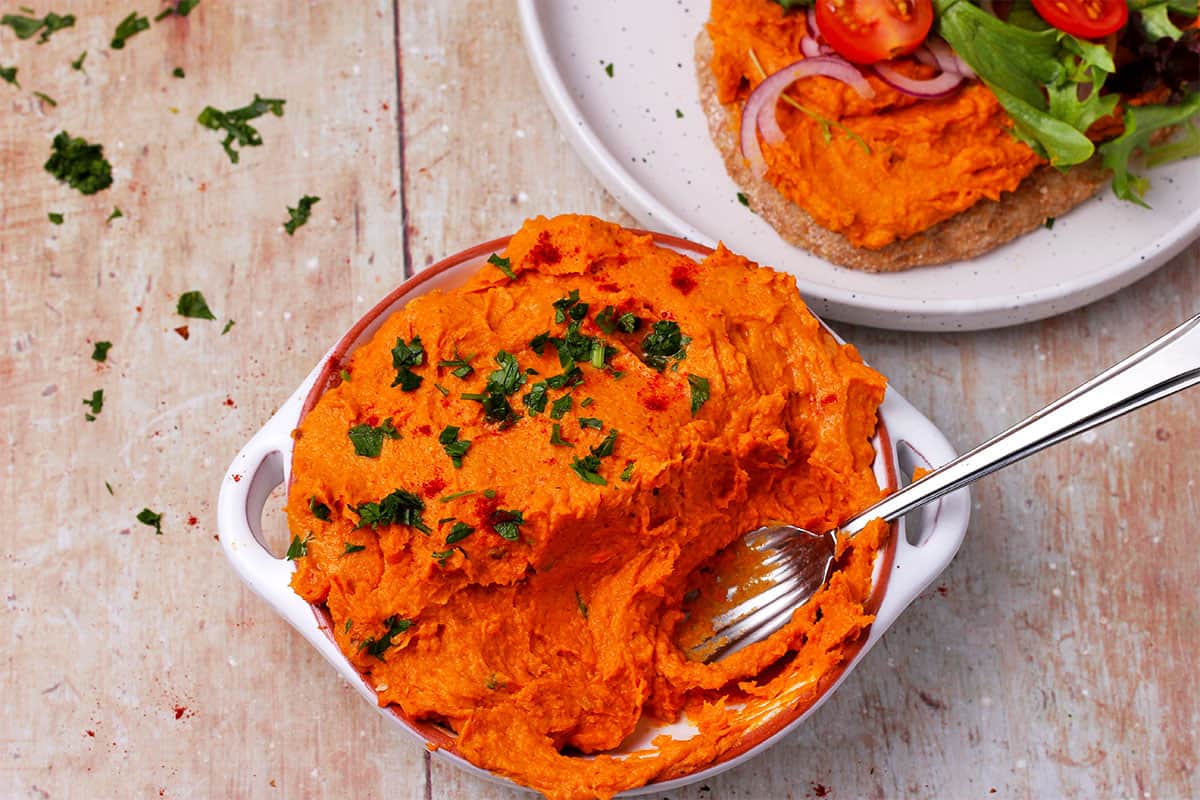 Sweet potato dip topped with chopped parsley in a bowl with a spoon.