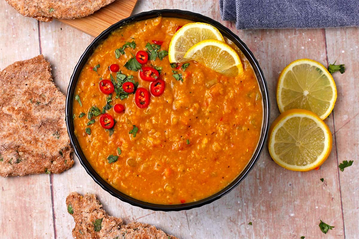 A bowl of mulligatawny soup (red lentil soup) with herbed flatbread and lemons.