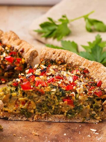 A piece of mushroom & kale quiche with diced red peppers and hazelnuts.