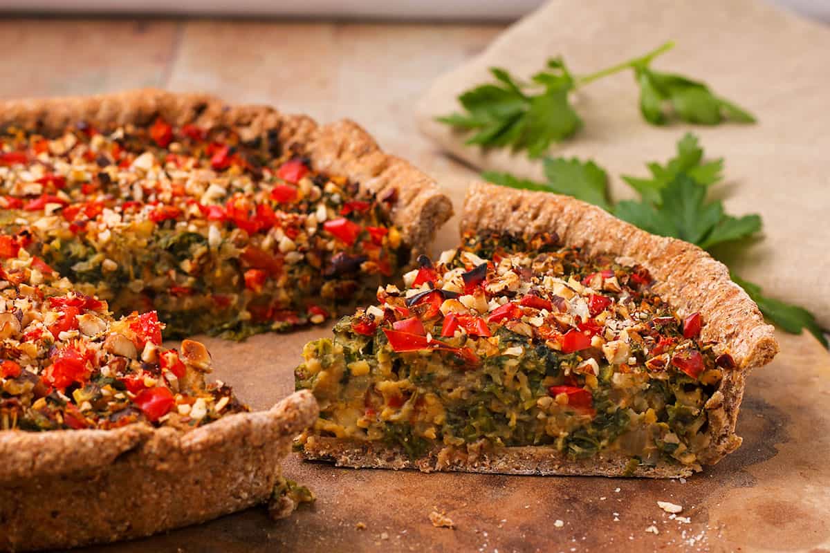 Vegan quiche with whole wheat crust is cut and placed on a stone.