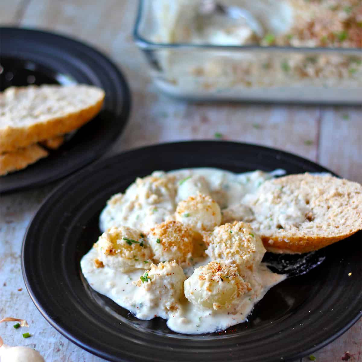 Creamy pearl onions on a black plate with bread.