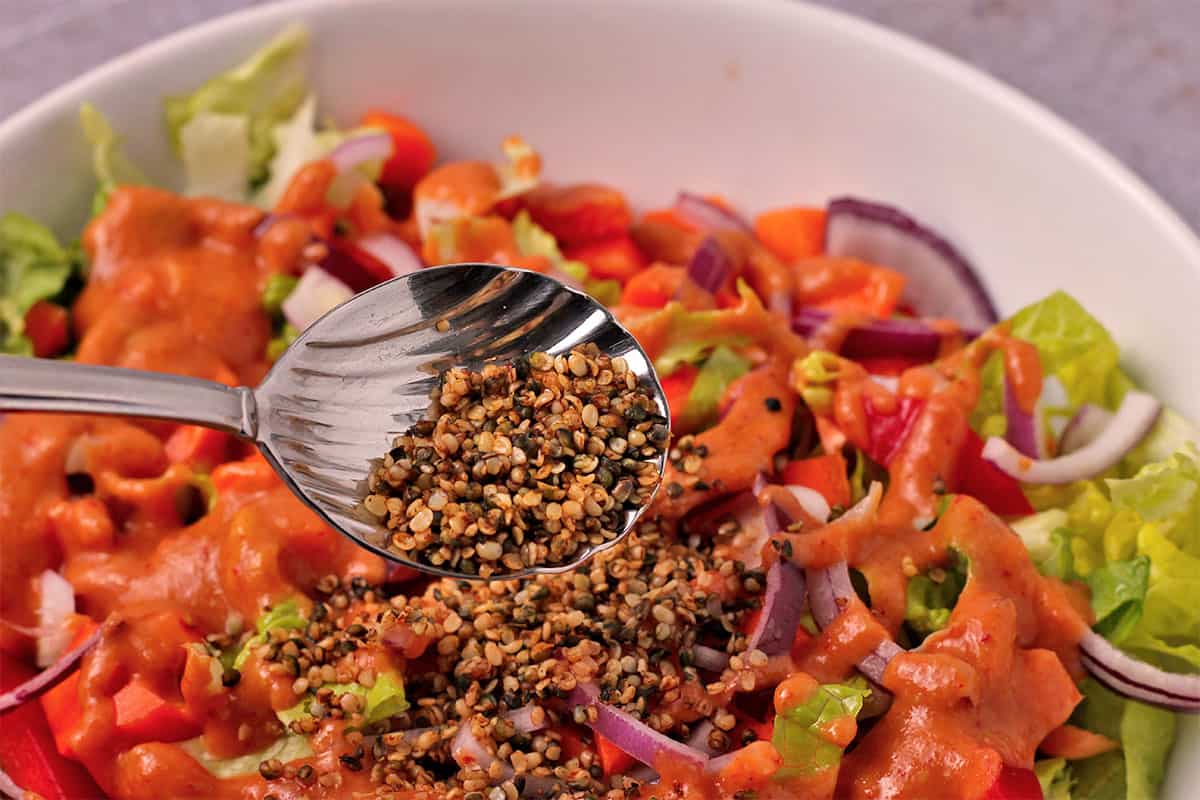 Hemp seed vegan bacon bits are sprinkled over a green salad with sriracha dressing.