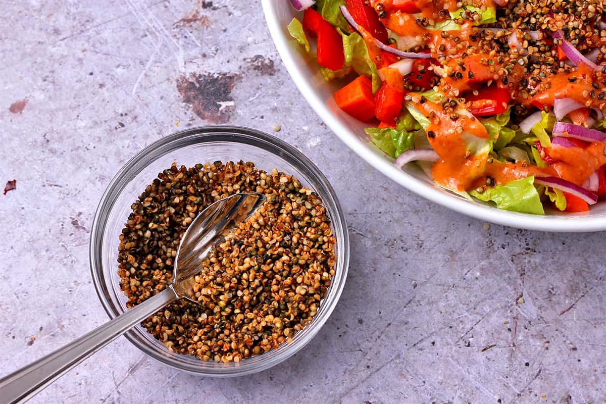 Vegan bacon bits with hemp seeds in a glass bowl with a spoon.