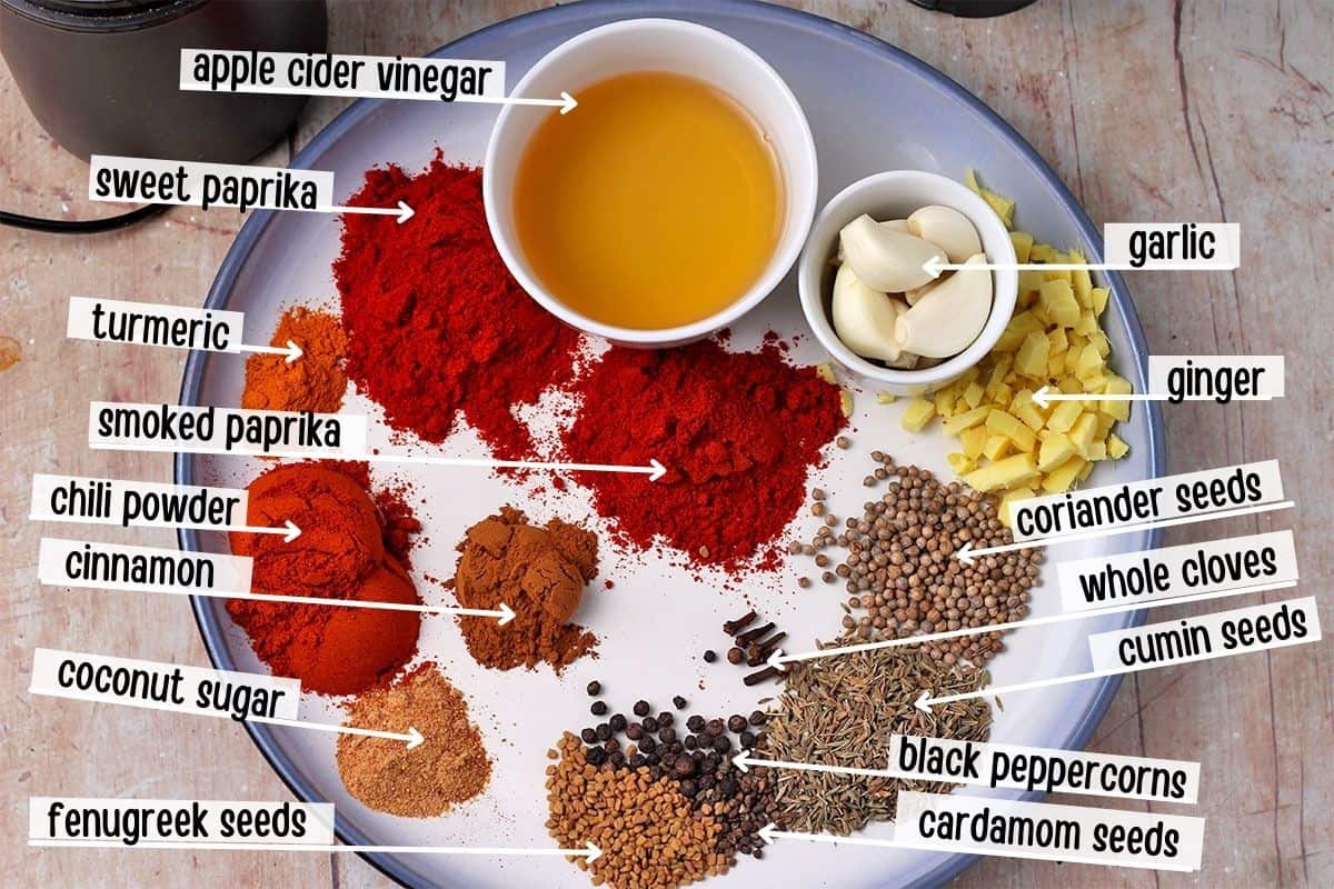 Each ingredient for homemade vindaloo paste is placed on a plate with labels for each ingredient.