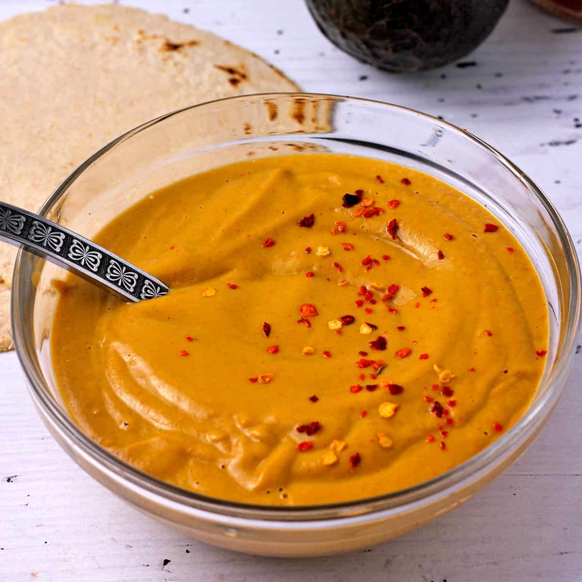 A glass bowl with chipotle avocado dressing with a spoon.