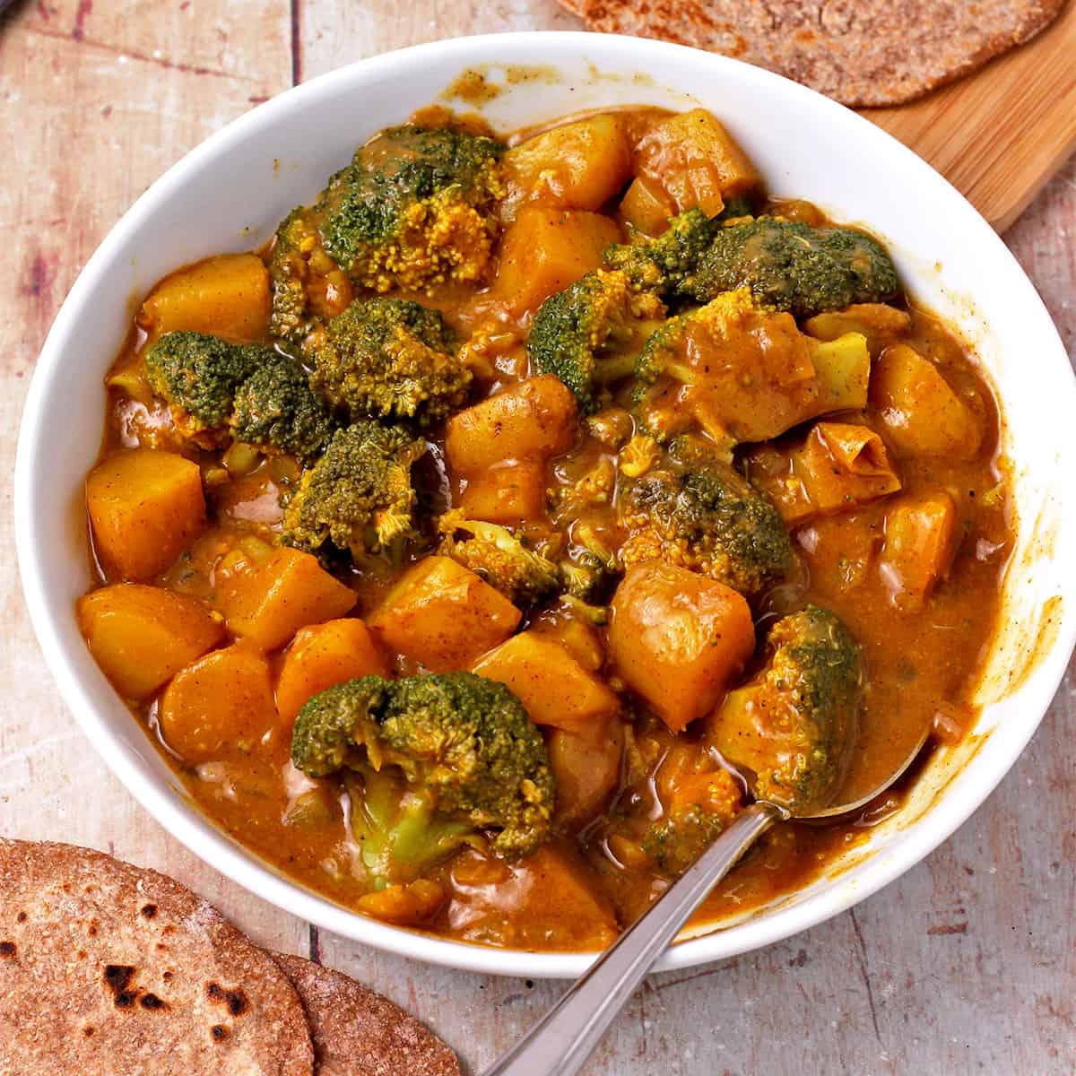 Potato and broccoli curry in a bowl with curry-gravy sauce in a white bowl with a spoon.