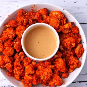 An overhead view of spicy air fryer cauliflower wings in a white bowl with peanut dipping sauce.