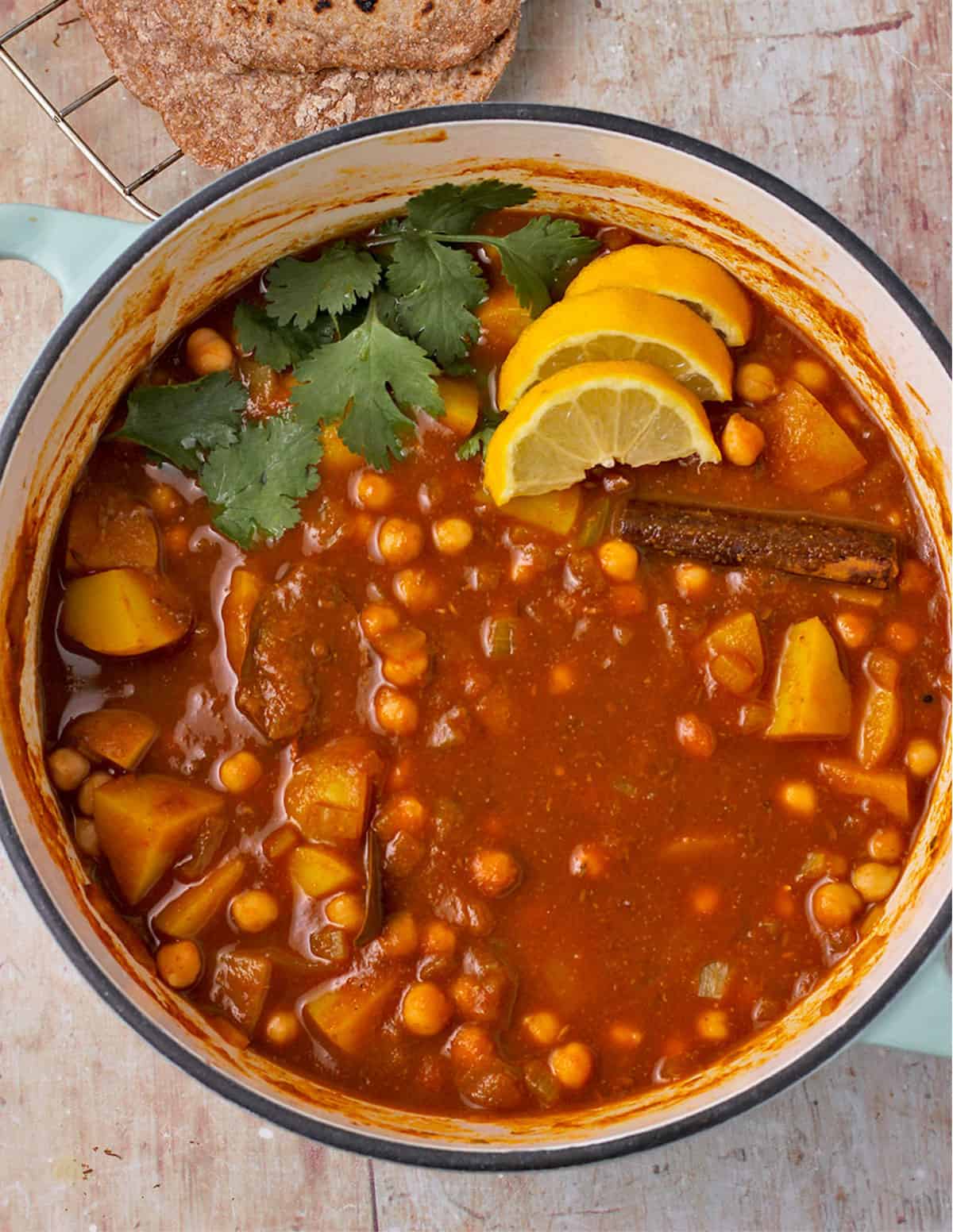 Chana Aloo, chickpea and potato curry in a pot garnished with cilantro and lemon wedges.