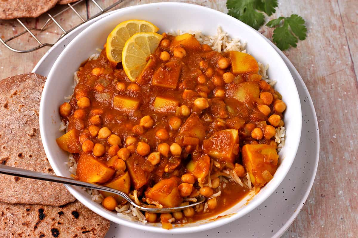 A bowl of chana aloo with rice and a spoon.