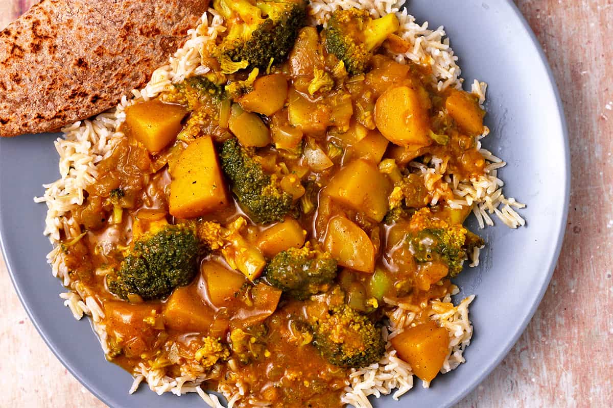 Potato and broccoli curry over rice on a blue plate.