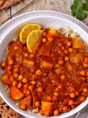 Overhead view of potato and chickpea curry in white bowl with brown rice.
