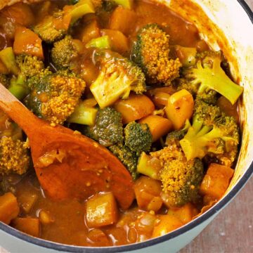 A pot of potato and broccoli curry with a wooden spoon.
