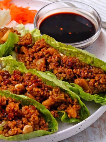 Vegan lettuce wraps with bulgur and firecracker dipping sauce on a white plate.