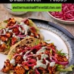 A plate with 2 cauliflower tacos with barbacoa paste, lettuce, red onions, and pepita sauce.