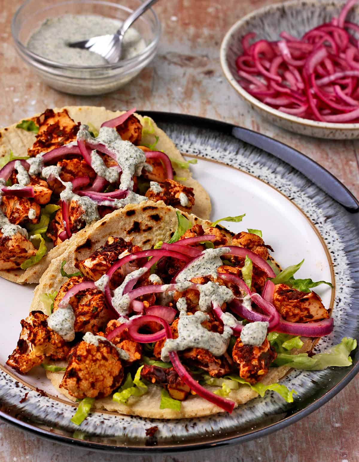 Roasted cauliflower tacos with pepita dressing, shredded lettuce, and pickled red onions.