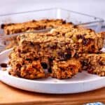 Oatmeal raisin bars are stacked on a white plate.