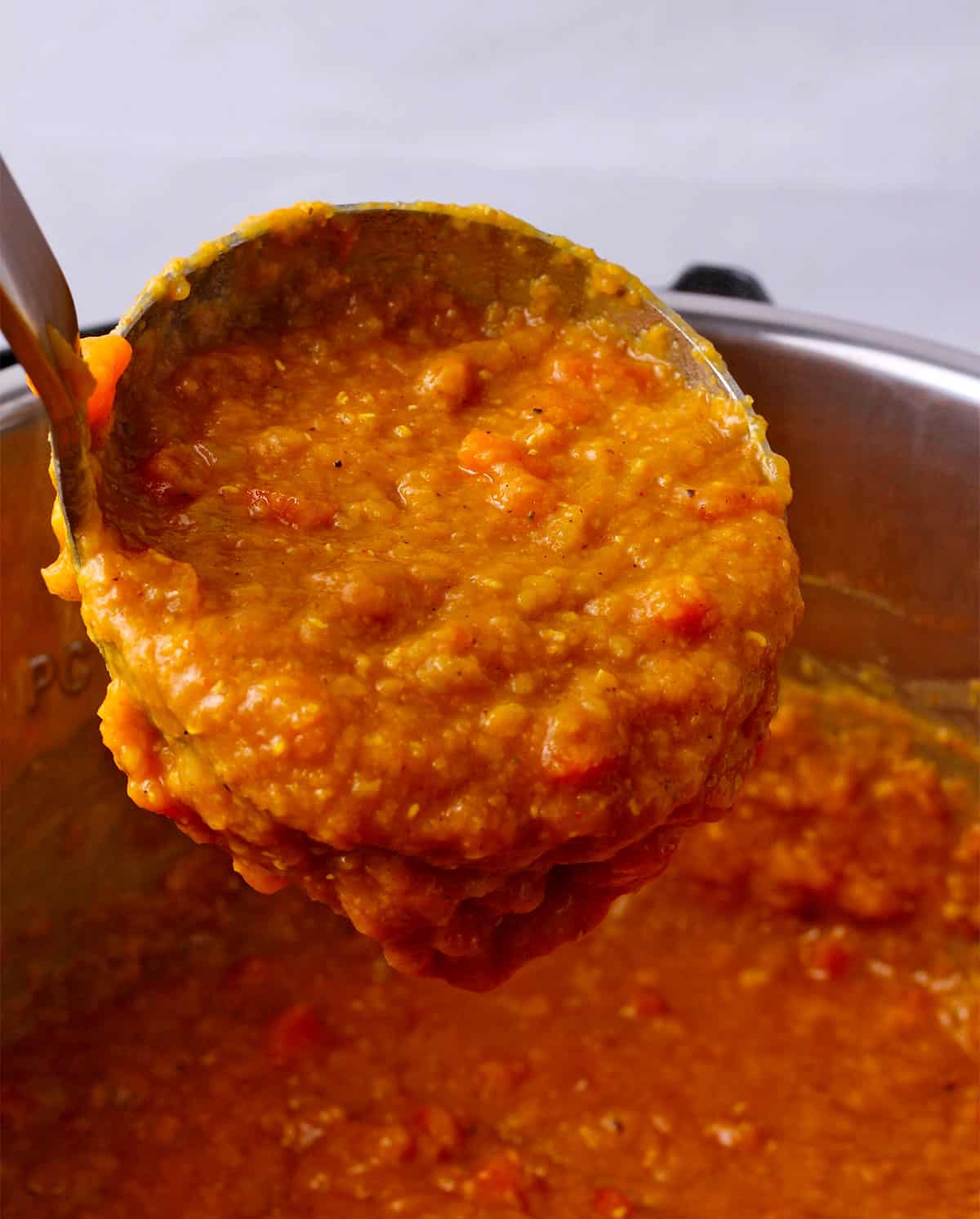 Red lentil soup in the Instant Pot is scooped in a ladle.