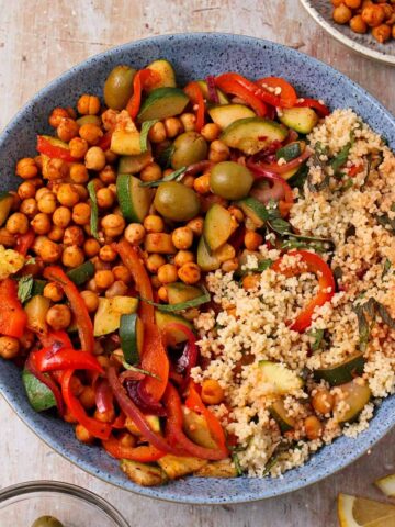 Moroccan chickpea salad with couscous, veggies, green olives, and mint in a blue bowl.