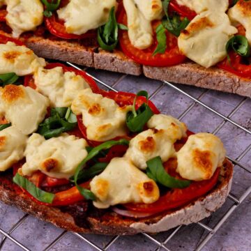 Browned vegan mozzarella dollops over tomatoes, onions, fresh basil over bread.