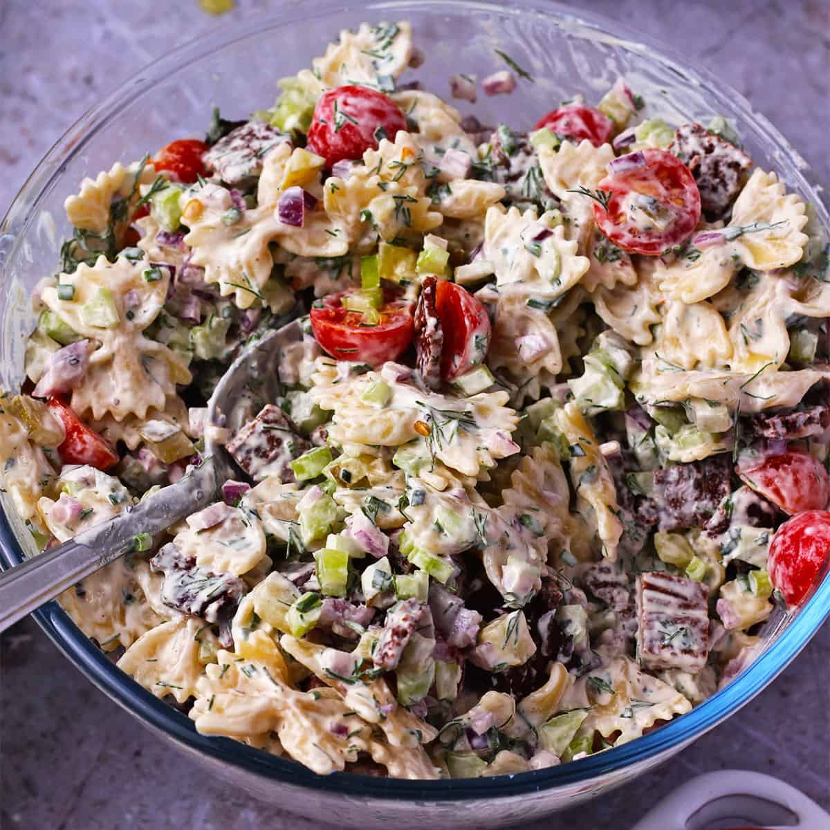 A bowl of vegan dill pickle pasta salad with tofu bacon, ranch dressing, tomatoes, celery, and red onions.