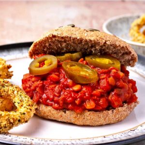 A lentil sloppy joe in a bun with onion rings on a plate.