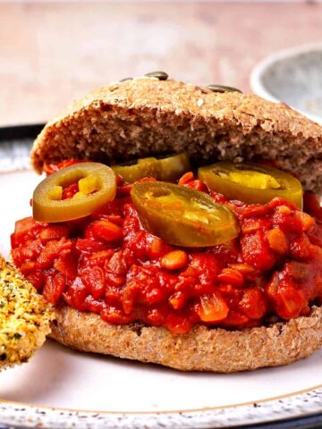 A lentil sloppy joe in a bun with onion rings on a plate.