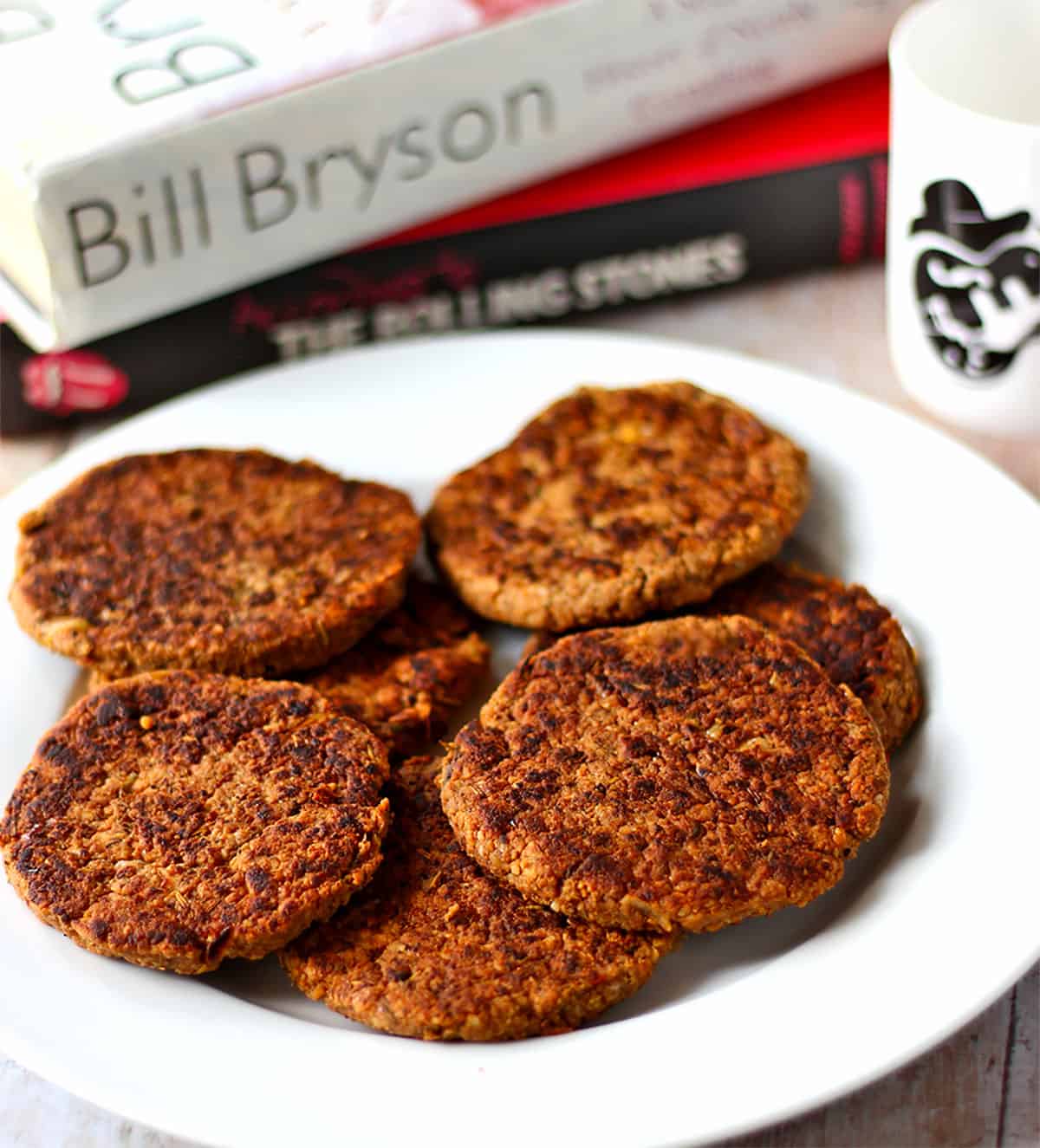 Tempeh sausage patties are stacked on a white plate.