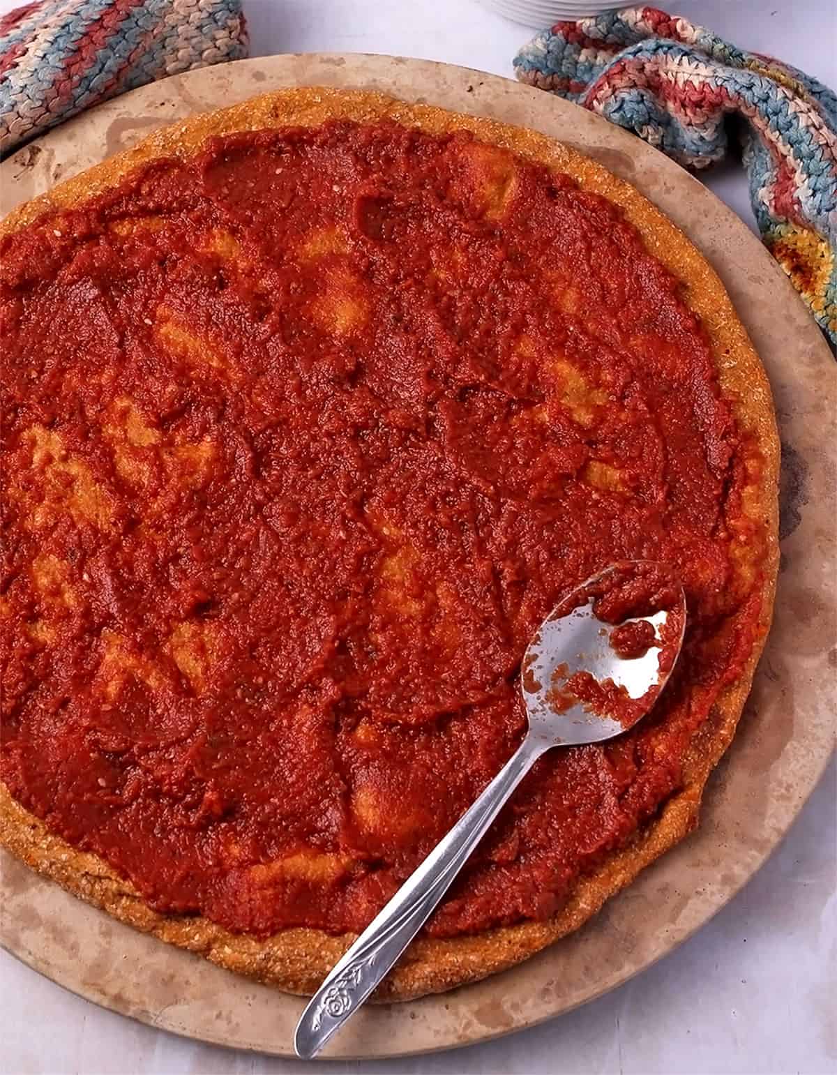 Tomato sauce is spread on a vegan sweet potato pizza crust.