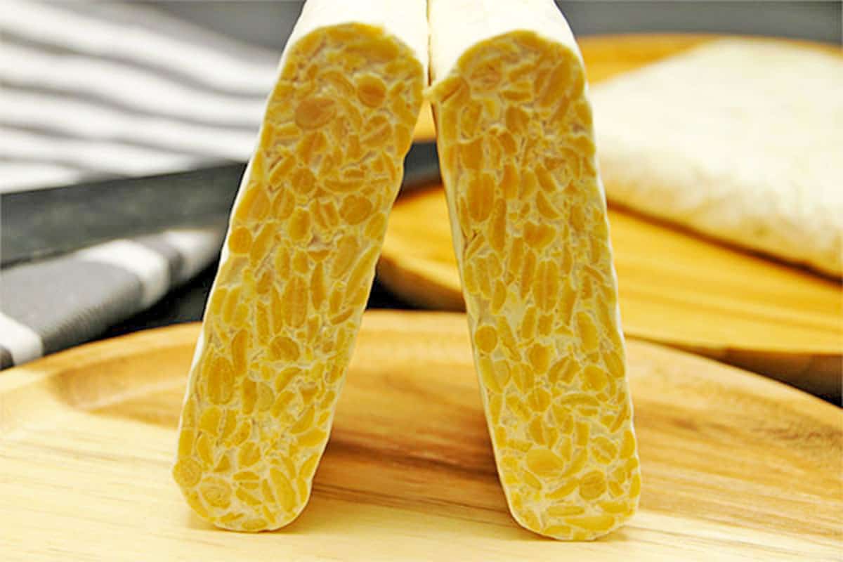 A raw tempeh block is cut in half and stood on end.